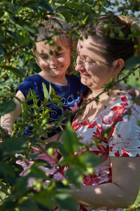 Smiling mother with daughter touching plants at agricultural field