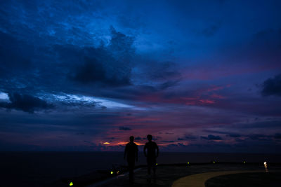 Silhouette people standing by sea against sky at sunset