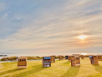 Hooded beach chairs on field against sky during sunset