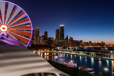 Illuminated ferris wheel by lake michigan against hancock building at dusk