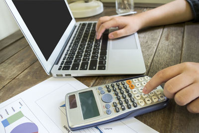 Cropped hands using calculator and laptop at table in office