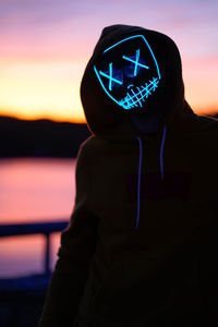 Man wearing neon mask while standing against orange sky