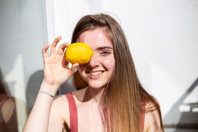 Portrait of smiling young woman holding lemon against wall
