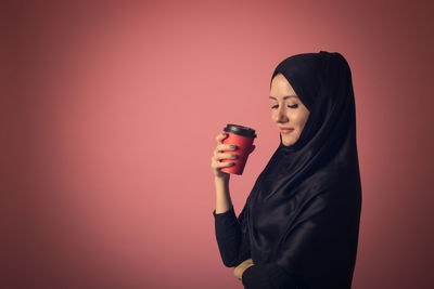 Young woman drinking glass against red background