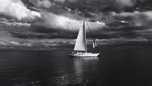 Sailboat sailing in sea against cloudy sky