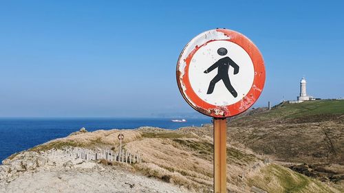 Road sign by sea against clear blue sky