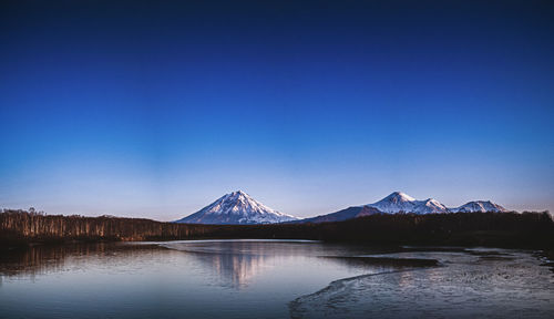 Scenic view of lake and mountains against clear blue sky