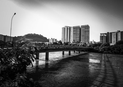 Bridge over river by buildings against sky