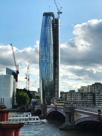 Bridge over river in city against cloudy sky