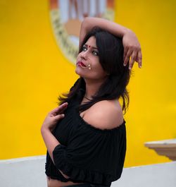 Beautiful young woman looking away against yellow wall