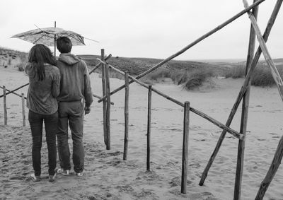 Rear view of couple standing with umbrella at beach