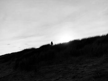 Silhouette man standing on sand dune against sky