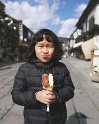 Portrait of girl having ice cream on street in town against sky