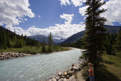 Woman standing by river in forest against sky