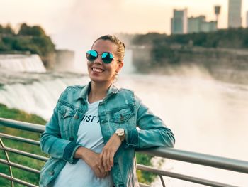 Portrait of smiling young woman standing against railing