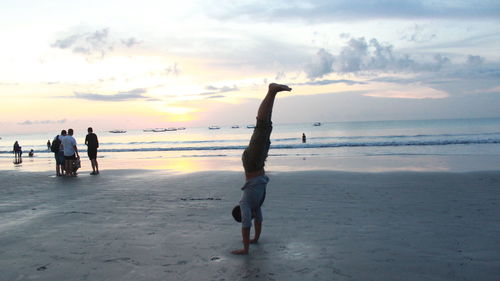 People at beach against sky during sunset