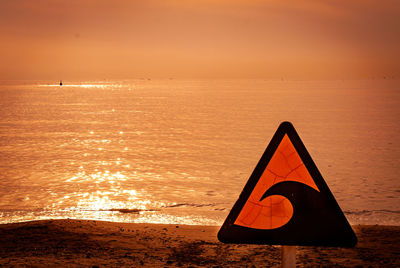 Information sign on beach against sky during sunset