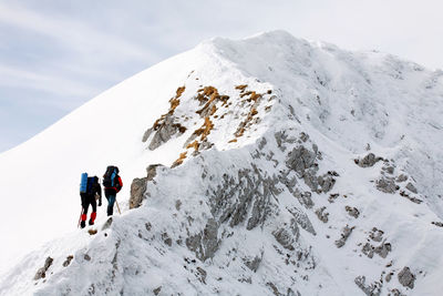 Low angle view of mountaineers climbing snowcapped mountain against sky