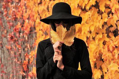 Young woman hiding face with autumn leaf