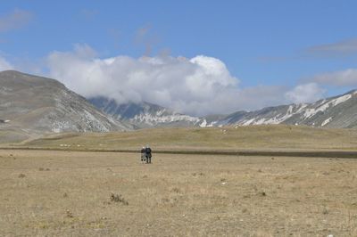 Scenic view of landscape by mountains against cloudy sky