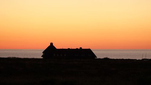 Silhouette building by sea against orange sky