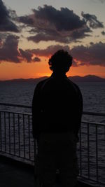 Silhouette of man standing by railing against sky during sunset