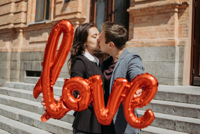 Couple holding balloon kissing outdoors