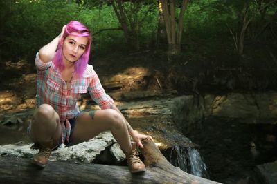 Portrait of young woman with dyed hair crouching on log in forest