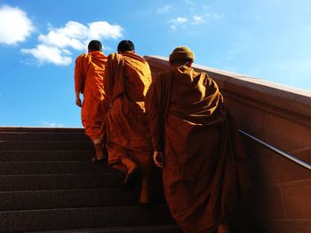 Rear view of monks walking on steps against sky