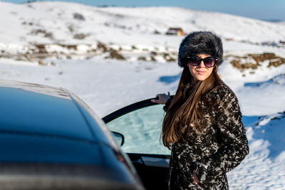 Portrait of woman standing by car on snow covered land