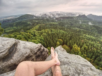 Man taking a break in nature and looking from summit down at the distant landscape.