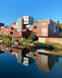 Reflection of buildings in lake against clear blue sky