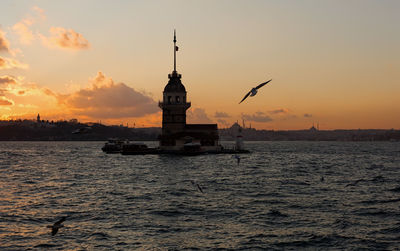 Silhouette lighthouse sailing on sea against sky during sunset