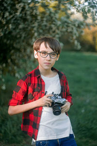 Portrait of boy holding camera while standing outdoors