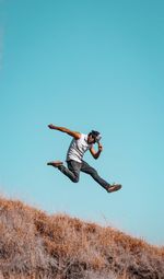 Low angle view of man jumping on field against clear blue sky