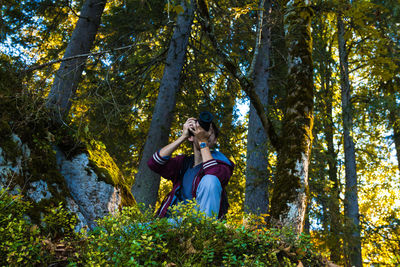 Low angle view of photographer against trees in forest