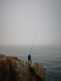 Man fishing in sea against clear sky