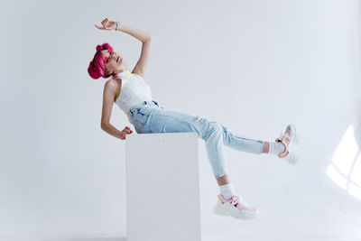 Side view of woman sitting on white wall