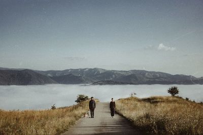 Rear view of couple walking on mountain against sky