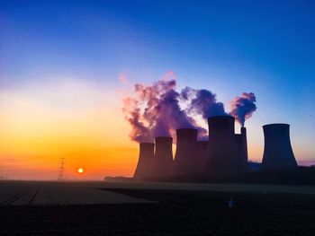 Smoke emitting from factory against sky at sunset