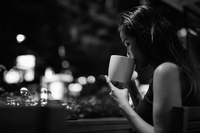 Side view of woman drinking coffee while sitting at cafe