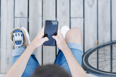 Teen male with leg prosthesis sitting on bench and browsing smartphone