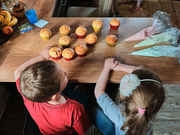 High angle view of kids sitting by table at home with cupcakes