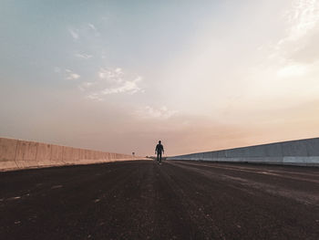 Rear view of man walking on road against sky