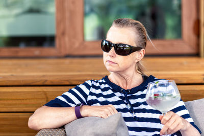 Middle-aged blonde woman with sunglasses relaxing in the garden with a cocktail in hand