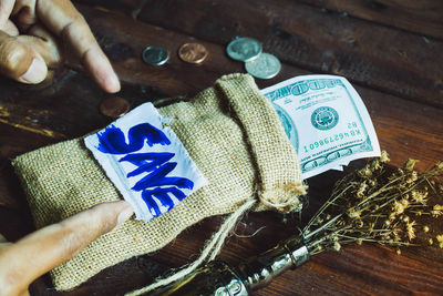 Cropped hands pointing at save text on sack with paper currency at table