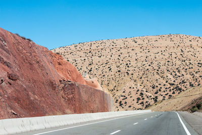 Road leading towards mountain against clear blue sky