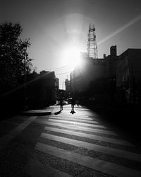 People walking on road in city against bright sun