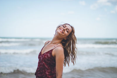 Young woman standing at beach against sky