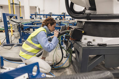 Engineer wearing reflective clothing analyzing machine part using flashlight in factory